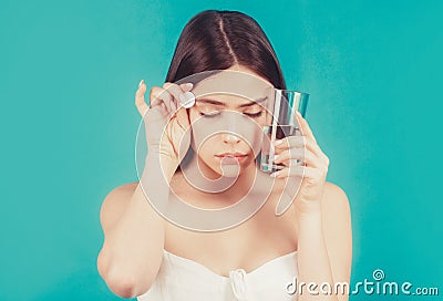 Woman taking drugs to releave headache. Brunette take some pills, holds glass of water, isolated on blue Stock Photo