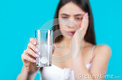 Woman taking drugs to releave headache. Brunette take some pills, holds glass of water, isolated on blue. Young woman Stock Photo