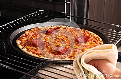 Woman taking out ready pizza out of the oven Stock Photo