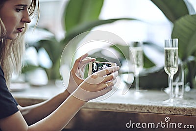 Woman taking photo of champagne in glasses. Meeting in city restaurant or cafe. Houseplants near window, daylight Stock Photo