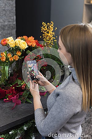 Woman taking pictures of flowers by her smartphone. The girl photographs the flowers that her lover gave her. A florist Stock Photo