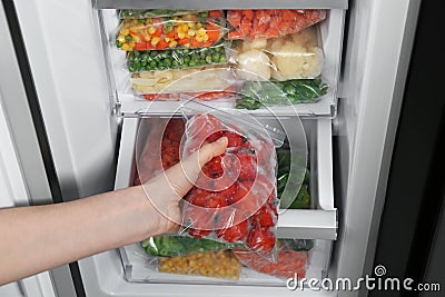 Woman taking plastic bag with frozen tomatoes from refrigerator Stock Photo