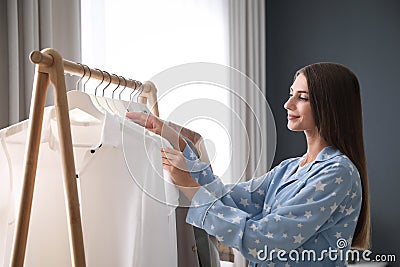 Woman taking shirt from rack with stylish clothes in room Stock Photo