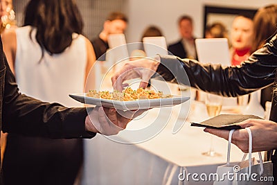 Woman taking snacks from the waiter on a fashion event party. Catering service concept. Editorial Stock Photo