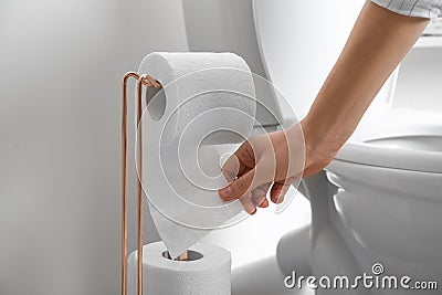 Woman taking toilet paper from roll holder in bathroom, closeup Stock Photo