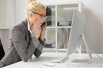 Woman talking on the phone and looking at computer in shock Stock Photo