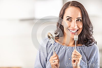 Woman thinking of eating something good bites into a fork while holding spoon in the other hand Stock Photo