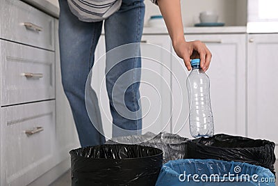 Woman throwing plastic bottle into trash bin in kitchen, closeup. Separate waste collection Stock Photo