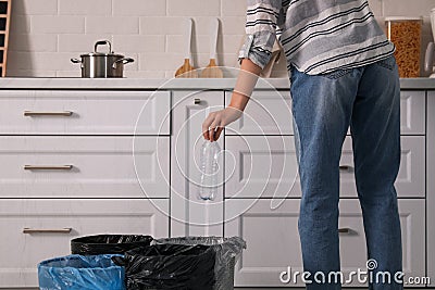 Woman throwing plastic bottle into trash bin in kitchen, closeup. Separate waste collection Stock Photo