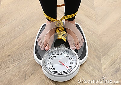 Woman tied with measuring tape using scale on floor, closeup. Overweight problem after New Year party Stock Photo