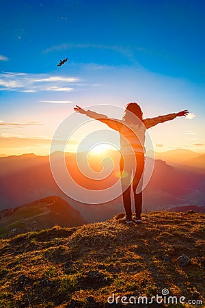 Woman on top of a mountain at sunset looks eagle Stock Photo