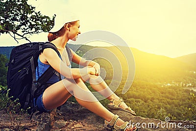 Woman tourist with a backpack sitting, resting on a mountain top on a rock on the journey Stock Photo