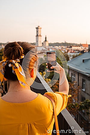 woman tourist looking at city on sunset from observation deck taking picture on her phone Stock Photo