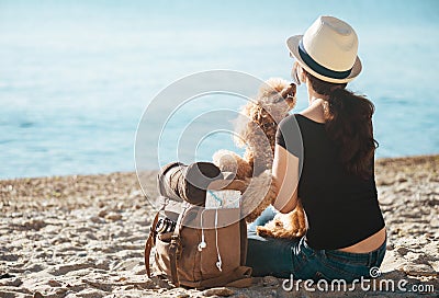 Woman traveler with backpack holding dog and looking at sea. Stock Photo