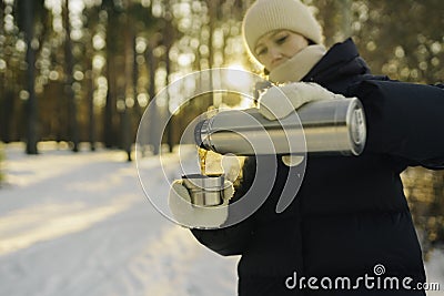 Woman traveler pours hot tea from a thermos into a mug Stock Photo