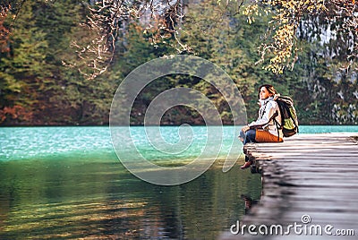 Woman traveler sits on wood bridge on mountain lake at sunny autumn day Stock Photo