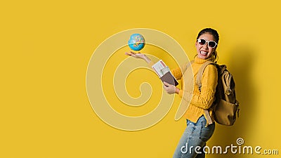 Woman traveler with suitcase, holding ball globe in the hand with passport and ticket on Yellow background. Portrait of smiling Stock Photo