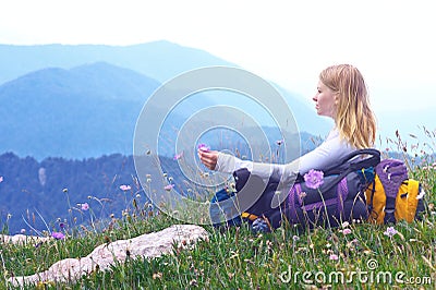 Woman Traveller with backpack sitting on grass with flowers relaxing Stock Photo