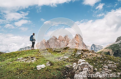 Woman trekker with backpack and trekking poles on green hill enjoying picturesque Dolomite Alps view near Tre Cime di Lavaredo Stock Photo