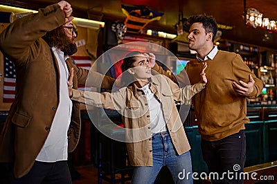 Woman trying to stop male friends fight at sport bar Stock Photo