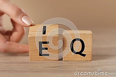 Woman turning cube with letters E and I near Q at wooden table, closeup Stock Photo