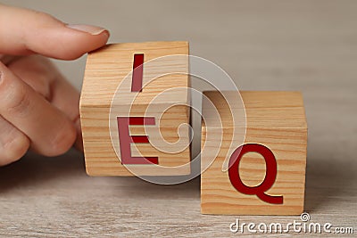 Woman turning cube with letters E and I near Q at wooden table, closeup Stock Photo