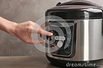 Woman turning on modern electric multi cooker on grey background Stock Photo