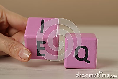 Woman turning pink cube with letters E and I near Q at white wooden table, closeup Stock Photo