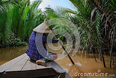Vietnamese woman with typical hat rowing a wooden boat through water palms on Mekong Delta, Vietnam Editorial Stock Photo