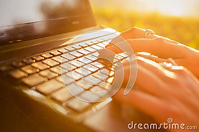 Woman typing on a laptop keyboard in a warm sunny day outdoors. Stock Photo