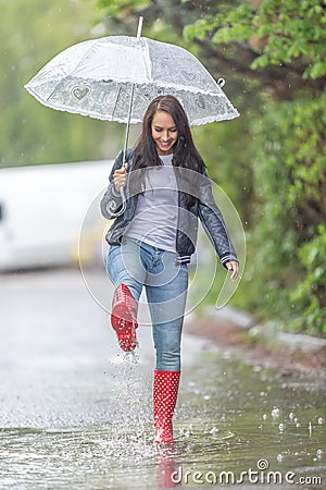 Woman with an umbrella walking in rainboots in a puddle under a heavy rain Stock Photo