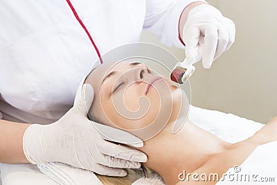 Woman undergoes the procedure of medical micro needle therapy with a modern medical instrument derma roller Stock Photo