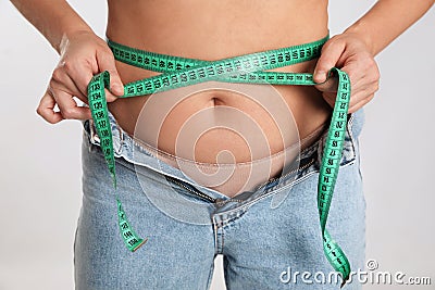 Woman in unfit jeans measuring her waist on light background, closeup. Weight loss concept Stock Photo