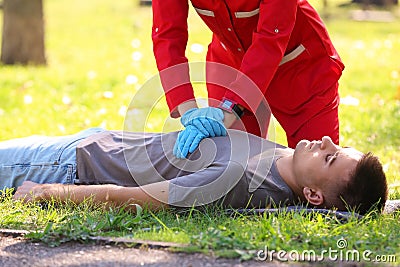 Woman in uniform performing CPR on unconscious man outdoors. Stock Photo