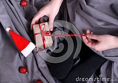 Woman is unwrapping gift box with red ribbon sitting in bed Stock Photo