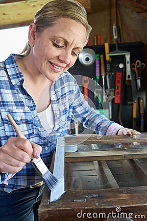 Mature Woman Upcycling Furniture In Workshop At Home Painting Cabinet Stock Photo