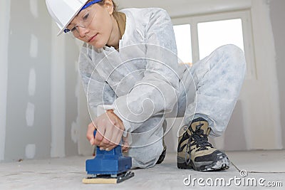 Woman uses electric sander on wood floor Stock Photo
