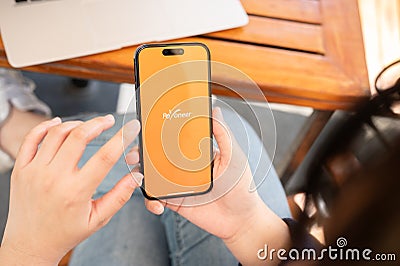 A woman uses the Payoneer application on her iPhone while sitting at a table in a cafe Editorial Stock Photo