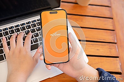 A woman uses the Payoneer application on her iPhone while working remotely at a cafe Editorial Stock Photo