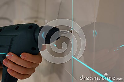 Woman using cross line laser level for accurate measurement and driving screw in tiled wall, closeup Stock Photo