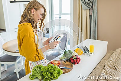 Woman Using Digital Tablet In Kitchen For Recipe Editorial Stock Photo