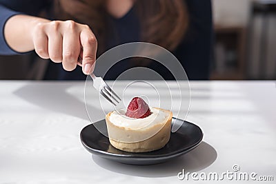 A woman using fork to cutting strawberry cheese tart on white vintage wooden table in cafe Stock Photo