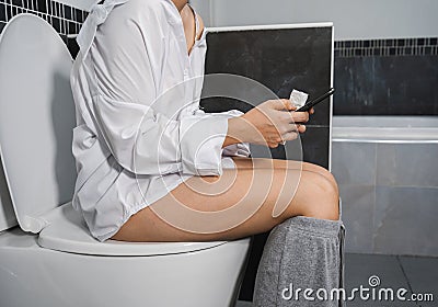 Woman using mobile phone and sitting on toilet Stock Photo