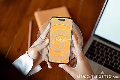 A woman using Payoneer application on her Iphone14 at her desk. Payoneer logo on Iphone14 screen Editorial Stock Photo