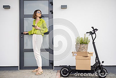 Woman with phone, electric scooter and packages going home Stock Photo