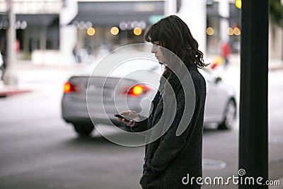 Woman Using a Smartphone App Waiting for a Rideshare Stock Photo