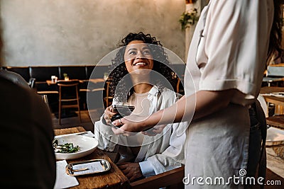 Woman using smartphone while paying restaurant bill with contactless payment during dinner party with friends Stock Photo