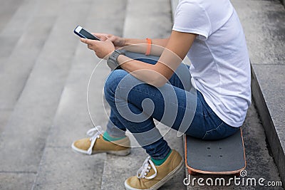 Woman using smartphone sit on skateboard Stock Photo