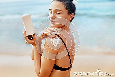 Woman using sunscreen on the shoulder holding sun cream bottle on the beach Stock Photo