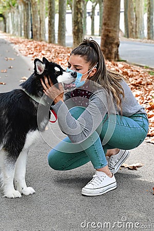 Woman using a surgical mask crouching down and holding a beautiful dog's head in the street Stock Photo